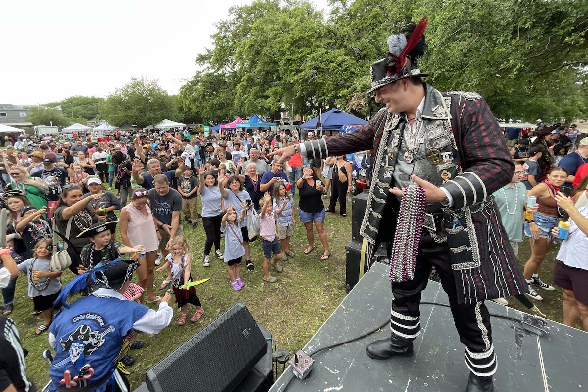 Man dressed as a pirate captain holding beads and interacting with a large crowd of people